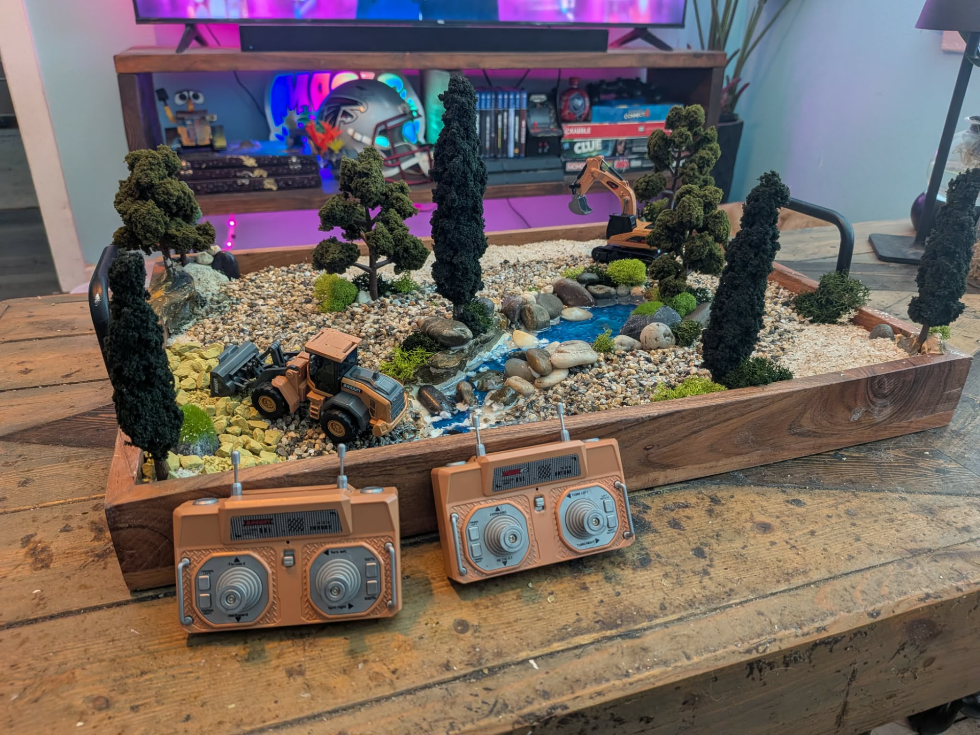 Finished RC dig site sitting on a workbench in a living room with two RC controllers