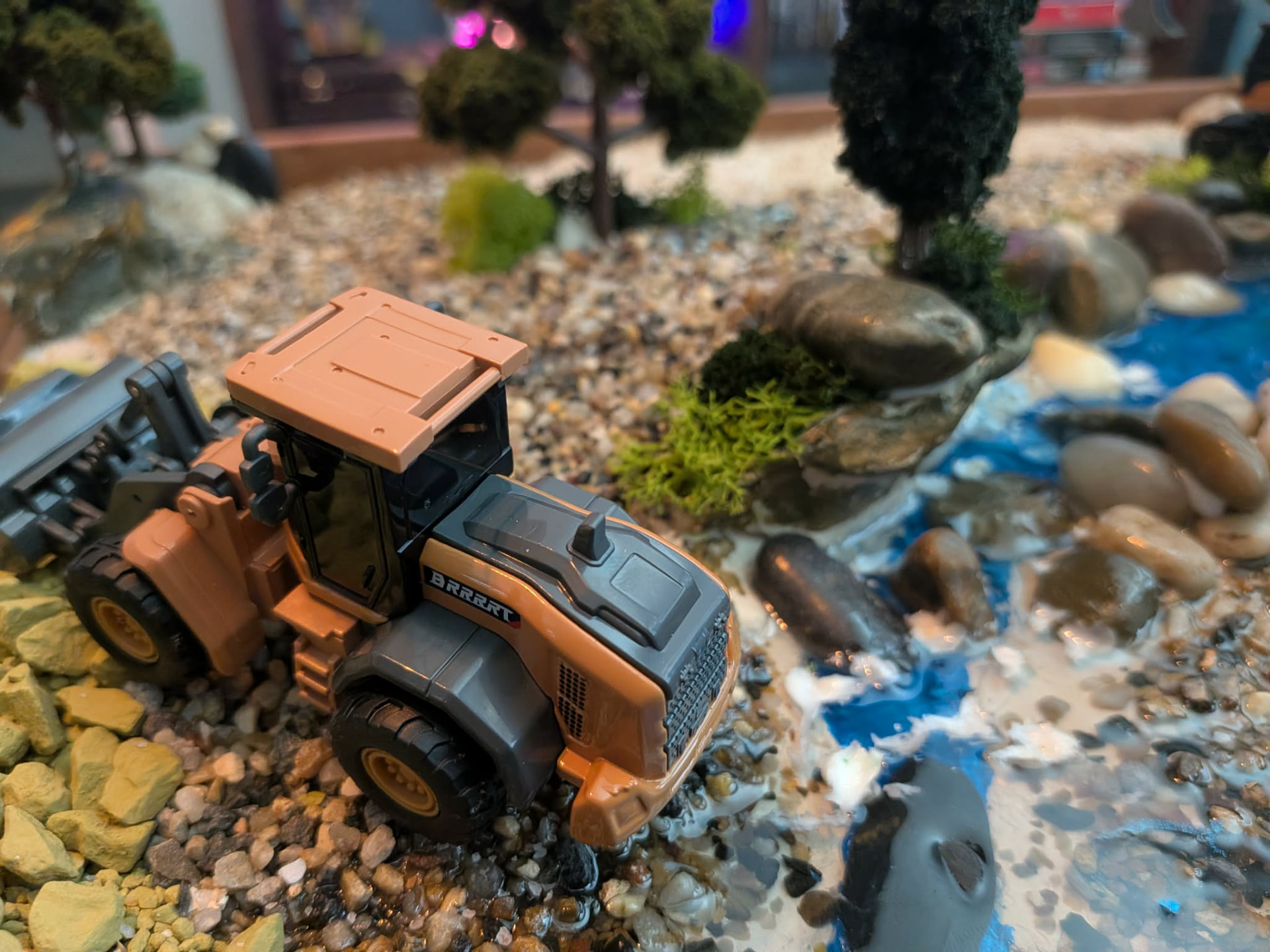RC wheel loader working a yellow rock pile beside the stream on a finished dig site